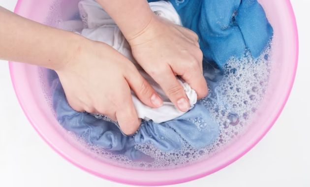 a person is washing a white piece of clothe in a light pink tube filled wit soapy water 