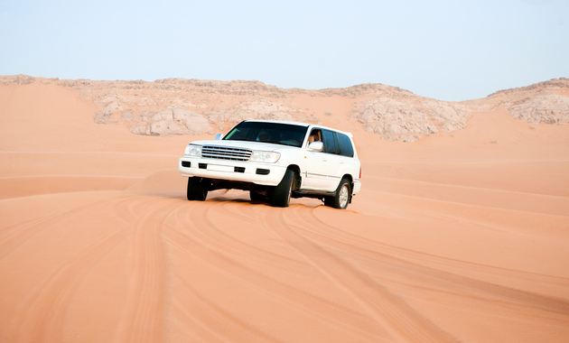 a white car in desert safari dubai with clear blue cloudy background