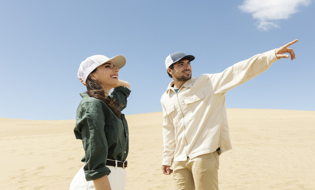 a boy is wearing a off white shirt and pant, a girl is wearing dark grey shirt with white pant and they both are standing in Dubai's desert