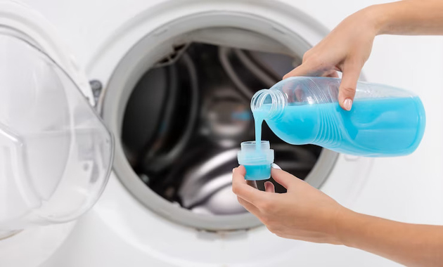 a woman is pouring liquid detergent in to the washing machine 