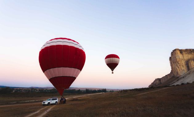 2 red colored hot air balloon in hilly and sandy area in dubai