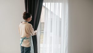 young woman standing near the window and fixing the curtains