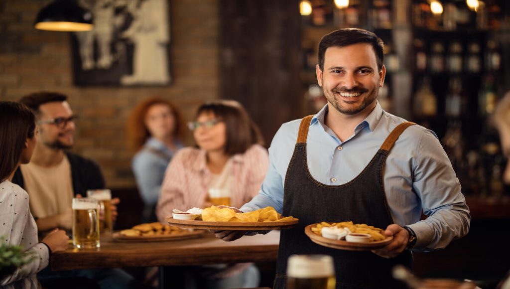 happy waiter holding-plates with food looking camera while serving guests restaurant