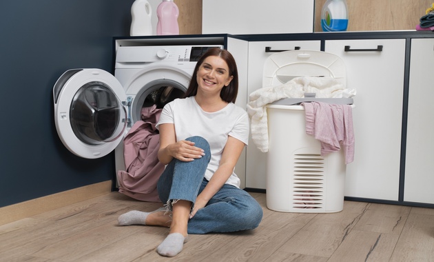 woman sitting washing machine with basket full clothes