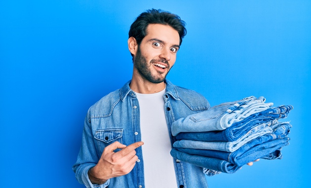 A man pointst towards jeans that he has been holding inm his other hand. 