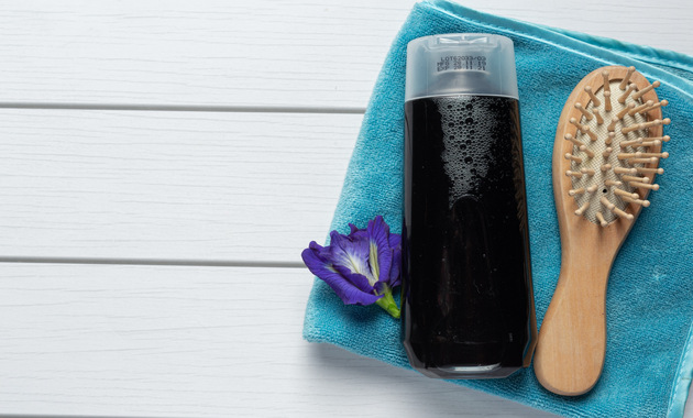 a shampoo bottle and wooden hair brush placed on a blue towel 