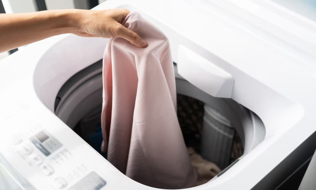 a girl is putting pink bed linen in dryer