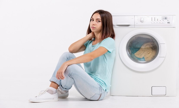 a girl is sitting next to washing machine