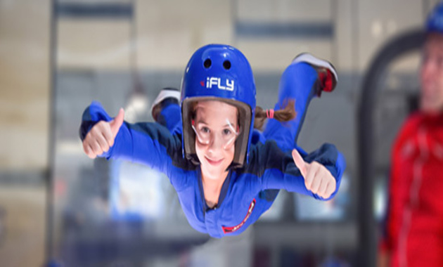 a kid wearing blue uniform and helmet and enjoying indoor sky diving in dubai