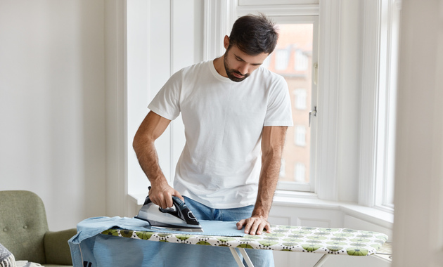 hard working bearded man ironing blue dress shirt