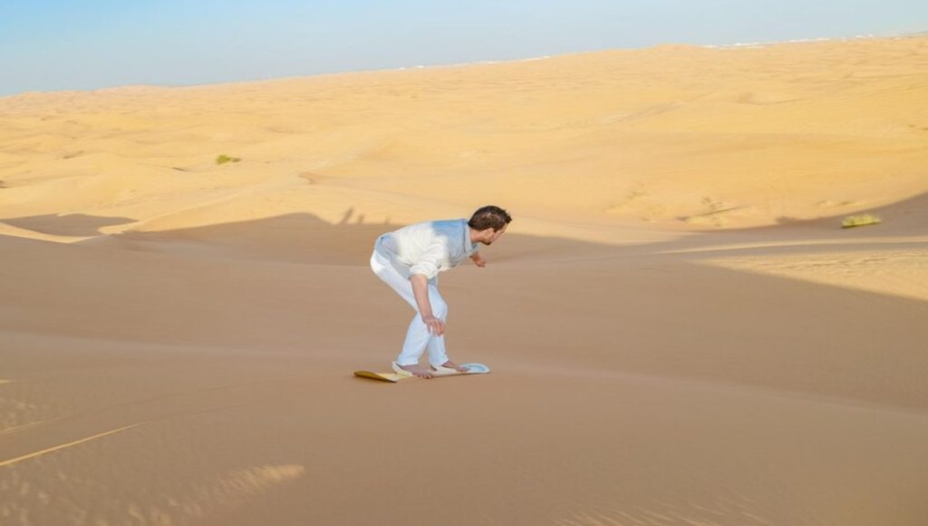 a man waering white shirt and pant is doing sandboarding in dubai