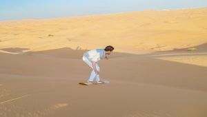 a man waering white shirt and pant is doing sandboarding in dubai