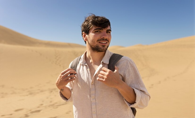 a man wearing a white shirt and holding a bagpack is standing in a desert 