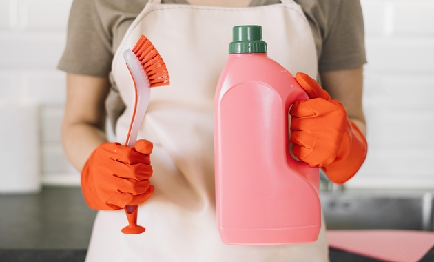 a women is holding liquid cleaning solution and cleaning brush to clean kitchen cabinets