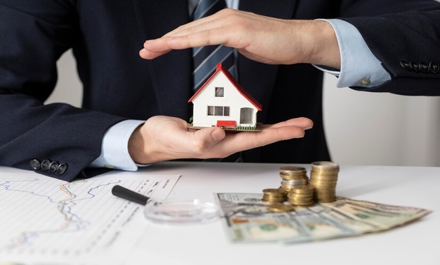 a man is holding a small house with some money placed over the table, the image represents buying property in Dubai